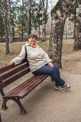 An elderly woman sits on a bench in a city park.