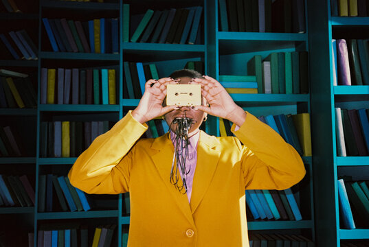 Unrecognizable woman in suit hiding face with cassette