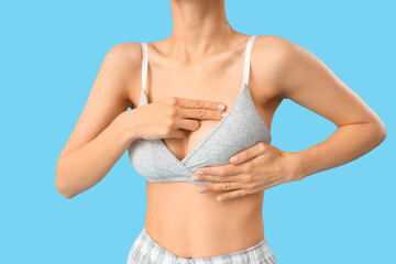 Young woman checking her breast on blue background, closeup. Cancer awareness concept