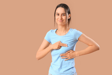 Young woman checking her breast on beige background. Cancer awareness concept