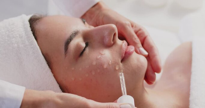 Beautician uses dropper to evenly apply serum to woman's face for optimal skin hydration and care. Close up of Caucasian woman's face during skin care treatment in spa salon. Skin care concept.