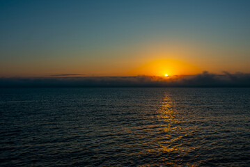 Fototapeta premium The sun rising over the sea behind a huge wall of fog 