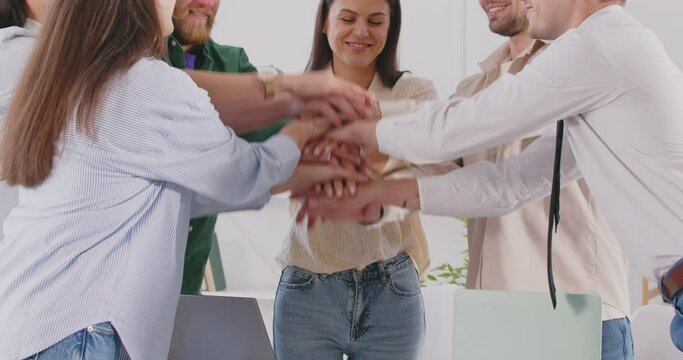 Happy smiling business people putting their arms together in a stack making deal or celebrating success standing at the desk on workplace in office. The concept of partnership and teamwork. 4k video.