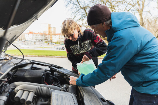 Senior couple putting water in coolant tank