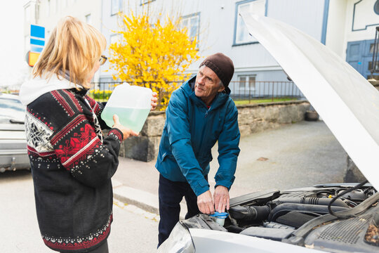 Senior couple putting water in coolant tank