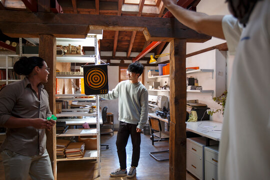 Group of coworkers playing darts in small office