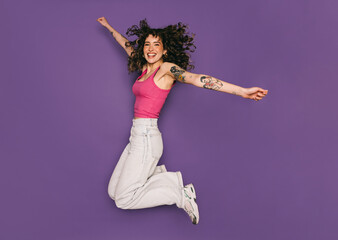 Joyful young woman jumping and celebrating on purple background