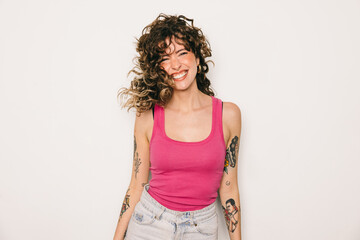 Joyful tattooed woman in pink top laughing against white background