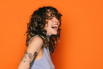 Joyful young woman laughing on bright orange background