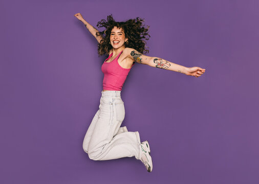 Joyful young woman jumping and celebrating on purple background
