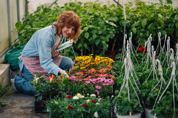 Happy botanist with checklist kneeling at hothouse and touching flowers