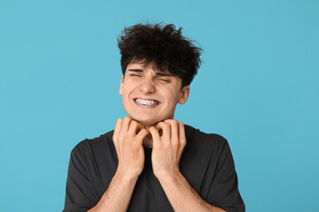 Young man with allergy scratching himself on blue background
