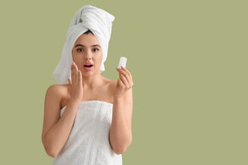 Surprised young woman in towel with crystal deodorant on green background