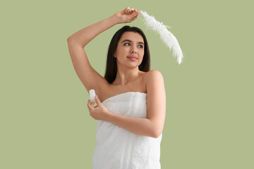 Beautiful young woman in towel with crystal deodorant and feather on green background