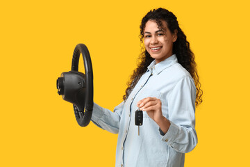 Beautiful young African-American woman with steering wheel and car key on yellow background
