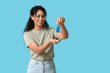 Beautiful young African-American woman with car key on blue background