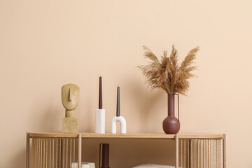 Wooden shelving unit with pampas grass in vase, candles and decor near beige wall in living room