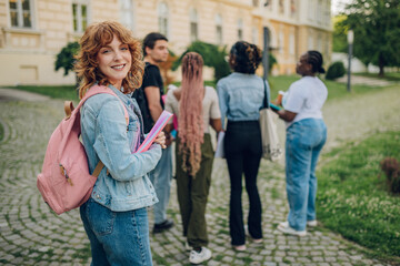 Portrait of happy student with textbook and backpack at campus.