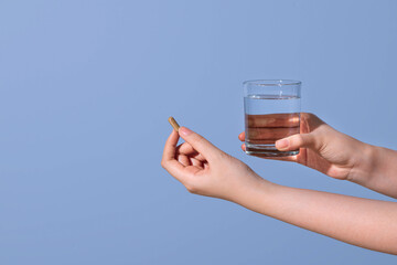 A woman's hand holding a fish oil capsule and holding a glass of water
