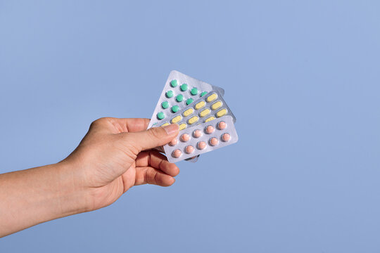 Female hand holding pills in blister packs on blue background