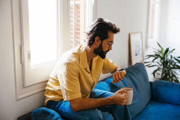 Man with cup of coffee using smartwatch at modern flat