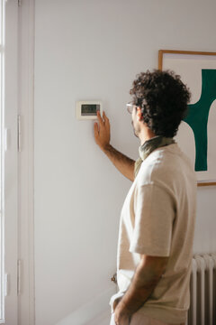 Man adjusting the temperature on the thermostat at home