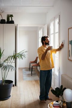 Man adjusting the temperature on the thermostat at home