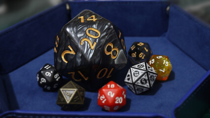 A black oversized D20 among an assortment of standard-sized dice on a blue tray taken with shallow...