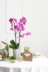 Beautiful table setting with orchid flower for wedding celebration near light wall