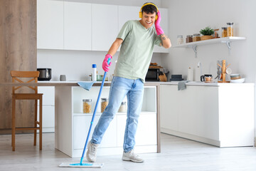 Young man with headphones and mop listening to music in kitchen