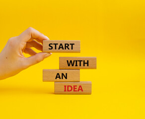 Start with an Idea symbol. Wooden blocks with words Start with an Idea. Beautiful yellow background. Businessman hand. Business and Start with an Idea concept. Copy space.