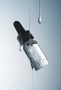 Clear glass dropper bottle suspended in air with liquid droplets. 