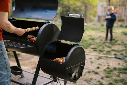 man grilling chicken shish kebab skewers on the bbq grill