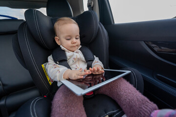 Small girl sitting in the child car seat using a digital tablet device during a long trip