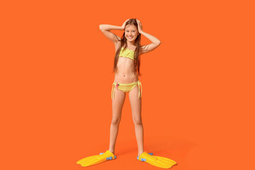 Cute little happy girl in swimsuit with flippers on orange background © Pixel-Shot