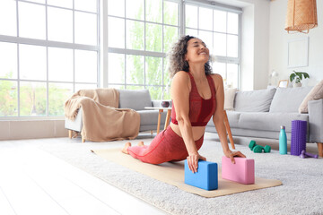 Sporty mature woman with blocks doing yoga on mat at home