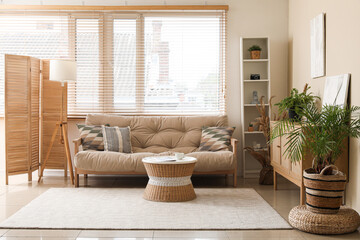 Stylish interior of living room with cozy sofa, chest of drawers, coffee table and houseplants