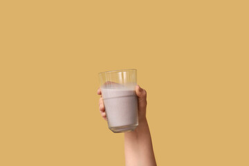 Female hand with glass of sweet chocolate milk on yellow background
