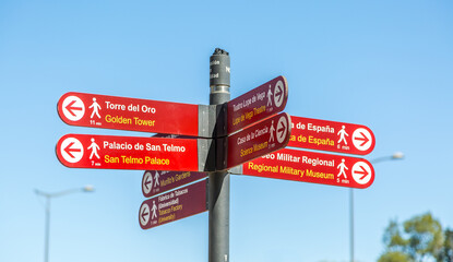 A red, metal sign-post pointing to many touristic attractions set against a blue sky in Seville, Spain