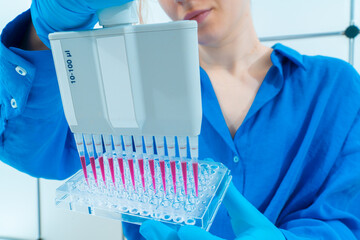 female genetic laboratory technician working with multi pipette and ninety-six well plate