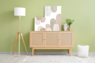 Wooden chest of drawers, lamp and beautiful pictures on green wall in room