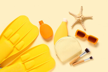 Beautiful composition with cosmetic bag, bottles of sunscreen and flippers on beige background