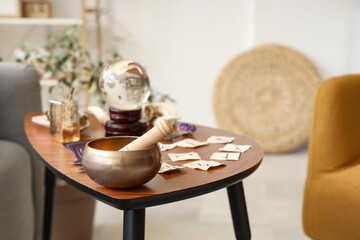 Tibetan singing bowl with witch's magic attributes on table in living room, closeup
