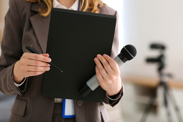 Beautiful young female reporter with microphone and notebook in office, closeup