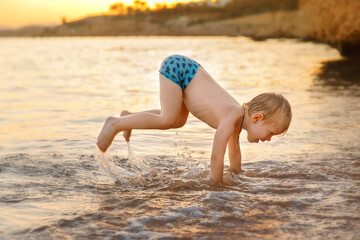 Fototapeta premium A boy playing in the sea water at the beach, jumping and goofing around, standing on his hands with his legs in the air.