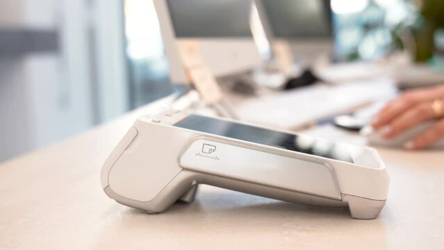 Pay by phone on electronic payment machine or card reader. E-money at cashless wallet. Female hand with pos-terminal and cellphone closeup. Client pays for the procedure in modern beauty clinic.