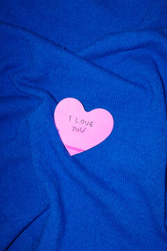 Heart-shaped I love you note on blue background with direct flashlight
