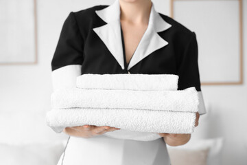 Chambermaid with stack of clean towels in hotel room, closeup