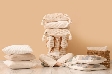 Young woman holding stack of pillows near beige wall