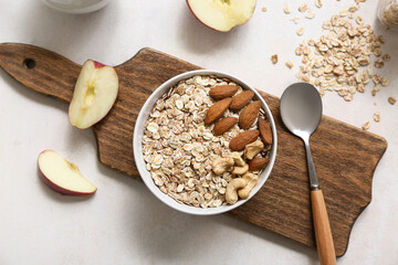 Wooden cutting board, apple, bowl with raw oatmeal and nuts on light background, closeup